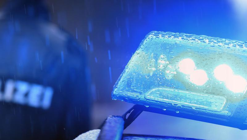 Ein Polizist steht im Regen vor einem Streifenwagen dessen Blaulicht aktiviert ist. Foto: Karl-Josef Hildenbrand/Archivbild
