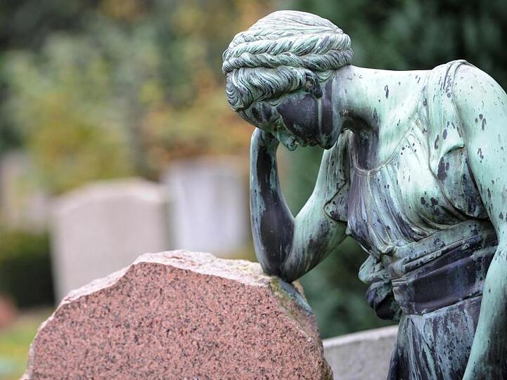 Eine Frauenfigur lehnt an einem Grabstein.