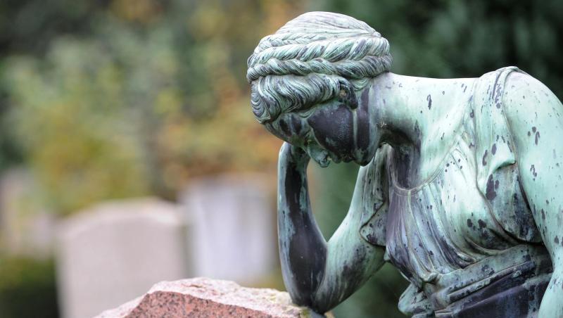 Eine Frauenfigur lehnt an einem Grabstein. Eine Frauenfigur lehnt an einem Grabstein.