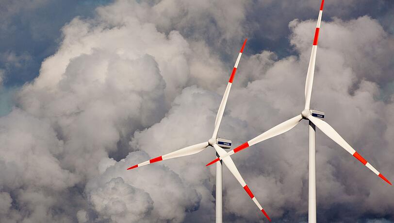 Windräder drehen sich vor den Kühltürmen eines Braunkohlekraftwerks.
