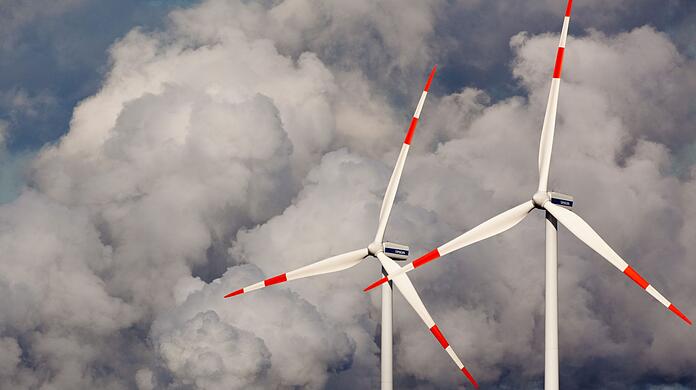 Windräder drehen sich vor den Kühltürmen eines Braunkohlekraftwerks.