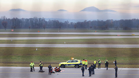 Vier Klimaaktivisten sitzen mit angeklebten Händen auf dem Zubringer einer Start-und Landebahn am Airport Franz-Josef-Strauß.