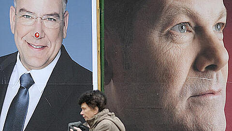 Eine Frau passiert in Hamburg die Wahlkampfplakate von Hamburgs Erstem Bürgermeister Christoph Ahlhaus (CDU, l) und seinem Herausforderer Olaf Scholz (SPD)