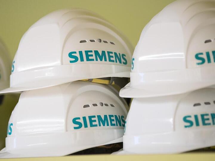 Weiße Schutzhelme mit dem Aufdruck "Siemens" liegen in einem Regal. Foto: Sebastian Kahnert/Archivbild
