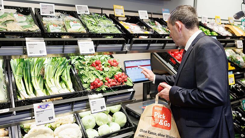 Der Bayerische Wirtschaftsminister Hubert Aiwanger (Freie Wähler) wiegt Gemüse während der Eröffnung der ersten vollautomatischen Rewe Pick&Go Filiale in München.