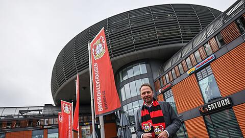 Uwe Richrath, Oberbürgermeister von Leverkusen, steht mit einem Fanschal vor dem Rathaus.
