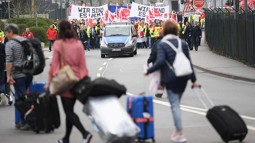 Während Flugreisende auf dem Weg zu einem Bus zum Flughafen Hahn sind, setzt sich ein Demonstrationszug nach einer Kundgebung am Frankfurter Flughafen in Bewegung. Mit einem Warnstreik der Gewerkschaft Verdi soll der Druck auf die Arbeitgeber im Bund und den Kommunen vor der nächsten Runde der Tarifverhandlungen erhöht werden.