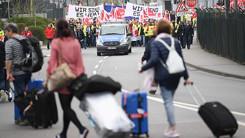 Während Flugreisende auf dem Weg zu einem Bus zum Flughafen Hahn sind, setzt sich ein Demonstrationszug nach einer Kundgebung am Frankfurter Flughafen in Bewegung. Mit einem Warnstreik der Gewerkschaft Verdi soll der Druck auf die Arbeitgeber im Bund und den Kommunen vor der nächsten Runde der Tarifverhandlungen erhöht werden.
