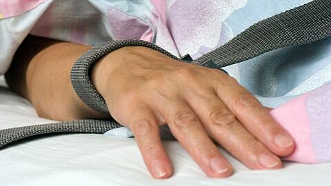 Eine mit einem Textilband festgebundene Hand eines Patienten - die Fixierung bzw. Fixation eines Patienten in der Krankenpflege durch Festschnallen am Handgelenk.