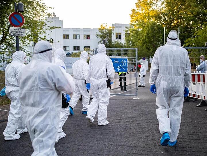 Beamte der Polizei und des Ordnungsamtes betreten in Schutzanzügen die Flüchtlingsunterkunft in St. Augustin.
