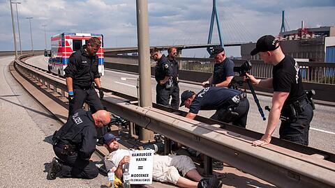 Polizisten versuchen auf der Köhlbrandbrücke zwei mit einem Eisenrohr miteinander verbundene Klimaaktivisten zu lösen.