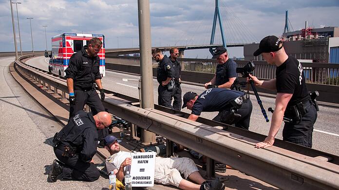 Polizisten versuchen auf der Köhlbrandbrücke zwei mit einem Eisenrohr miteinander verbundene Klimaaktivisten zu lösen.