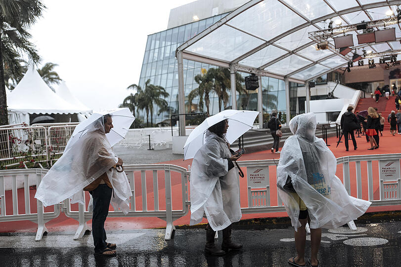 Menschen gehen im Regen auf dem 78. Internationalen Filmfestival in Cannes am Festivalpalast vorbei.