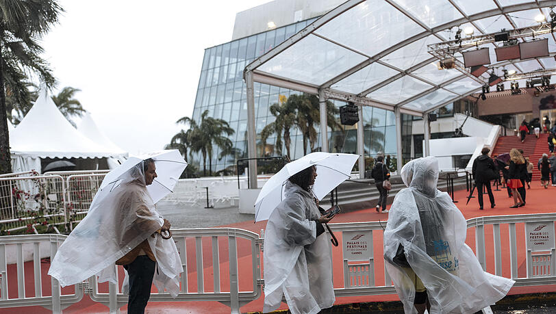 Menschen gehen im Regen auf dem 78. Internationalen Filmfestival in Cannes am Festivalpalast vorbei. Menschen gehen im Regen auf dem 78. Internationalen Filmfestival in Cannes am Festivalpalast vorbei.
