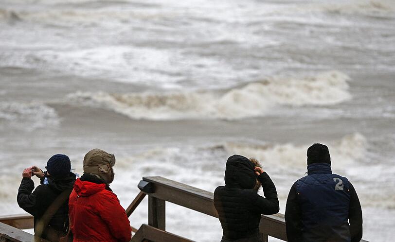 Spaziergänger betrachten in Wenningstedt die aufgewühlte Nordsee.