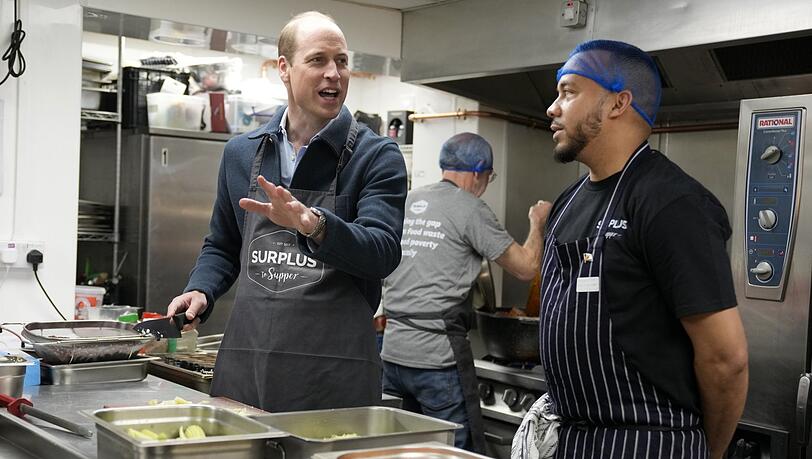 Kaum ist er wieder da, hilft er in der Küche aus: Der britische Prinz William hilft dem Chefkoch Mario Confait (r.) bei der Herstellung von Bolognese-Soße während eines Besuchs bei Surplus to Supper.