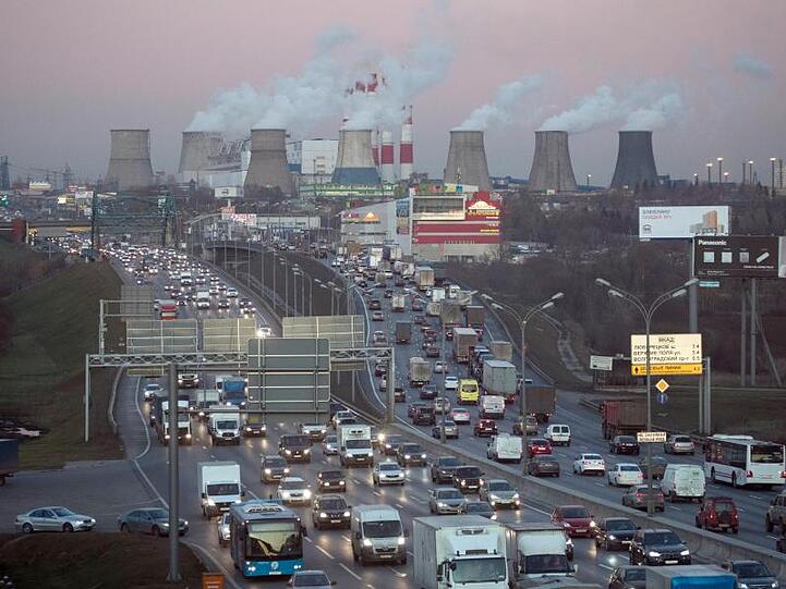 Kein Zustand auf Dauer: Verkehrsstau auf einer großen Straße in Moskau, im Hintergrund qualmen große Kraftwerke.