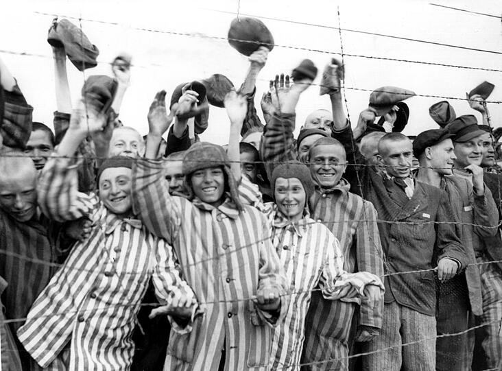 Hinter Stacheldraht eingepferchte überlebende KZ-Häftlinge jubeln in Dachau ihren amerikanischen Befreiern zu.