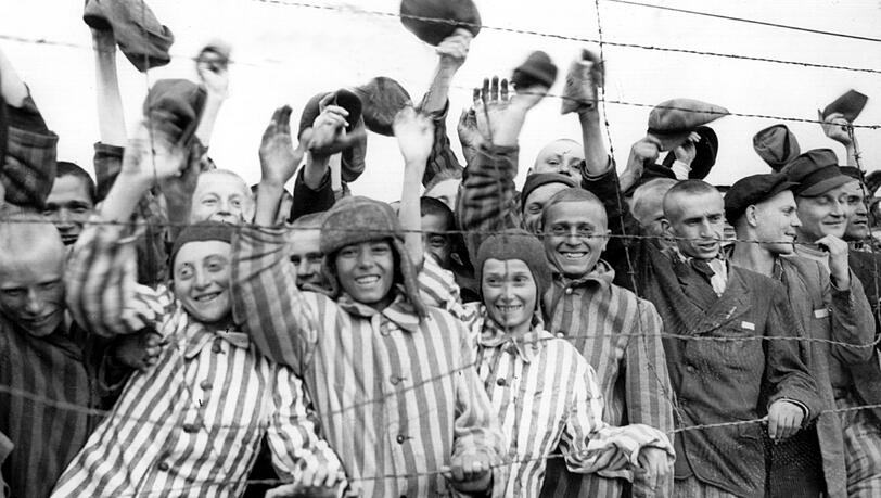 Hinter Stacheldraht eingepferchte überlebende KZ-Häftlinge jubeln in Dachau ihren amerikanischen Befreiern zu. Hinter Stacheldraht eingepferchte überlebende KZ-Häftlinge jubeln in Dachau ihren amerikanischen Befreiern zu.