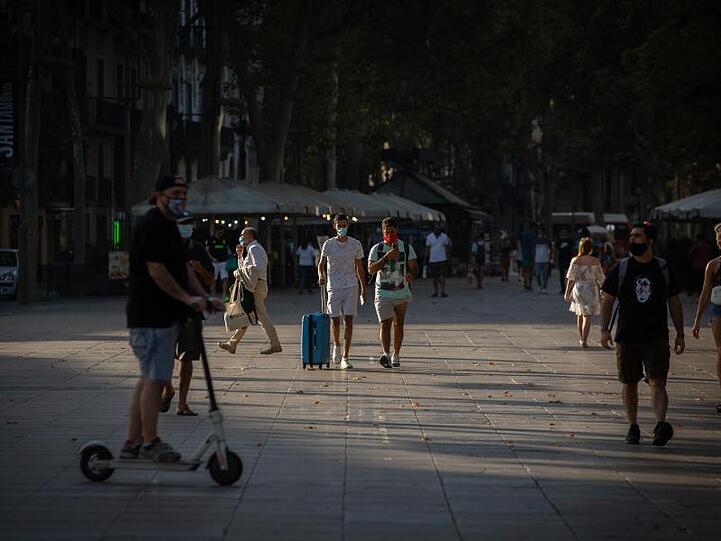 Menschen, manche von ihnen mit Mundschutz, gehen auf der langen Promenade La Rambla in Barcelona entlang.