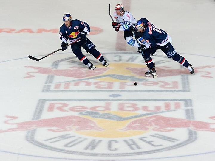 Spieler kämpfen um den Puck. Auf dem Boden ist das Logo des EHC Red Bull zu sehen. Foto: Andreas Gebert/dpa/Archivbild