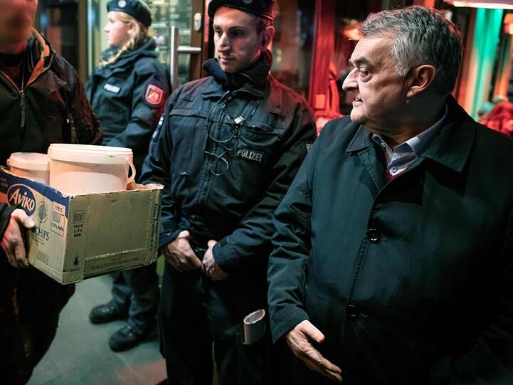 Herbert Reul (r), Innenminister von Nordrhein-Westfalen, verfolgt, wie nach einer Razzia Beweismittel aus einer Shisha-Bar getragen werden.