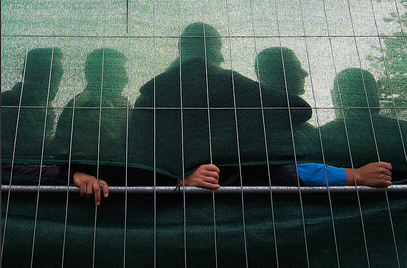 Flüchtlinge stehen hinter einem Zaun einer Asylunterkunft in Hamburg (Symbolbild).