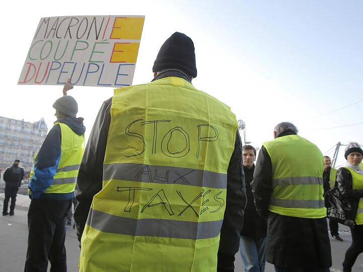 Demonstranten in gelben Warnwesten protestieren in Frankreich gegen hohe Spritpreise. Auf dem Plakat steht sinngemäß: "Macron, du nimmst von den Leuten".