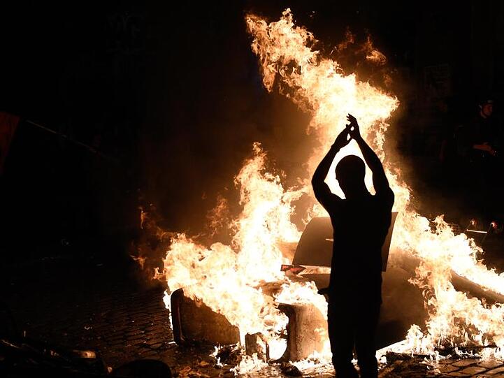 Ein Demonstrant wirft Holzstücke in eine brennende Barrikade.