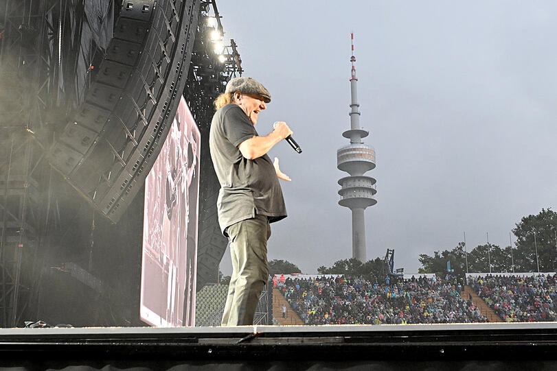 Brian Johnson strahlt mit Schiebermütze und schlichtem Polohemd  Kumpelhaftigkeit pur aus.