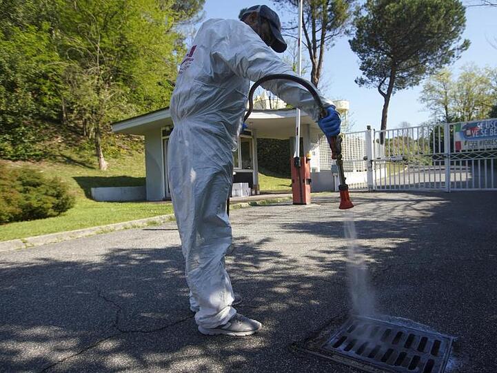 Ein Arbeiter in einem Schutzanzug sprüht Desinfektionsmittel auf ein Kanalisationsgitter in einem Privatviertel Roms. Italien bereitet sich auf eine teilweise Wiedereröffnung nach den langen Ausgangsbeschränkungen vor.