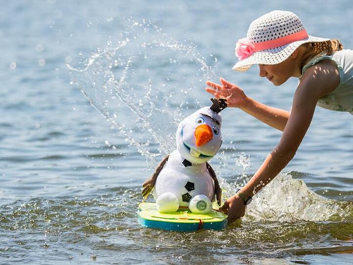 Der kann's besonders gut brauchen: Die kleine Lilith erfrischt ihren Stoff-Schneemann Olaf, Figur aus dem Disney-Film "Die Schneekönigin", mit Wasser aus dem Main bei Flörsheim.