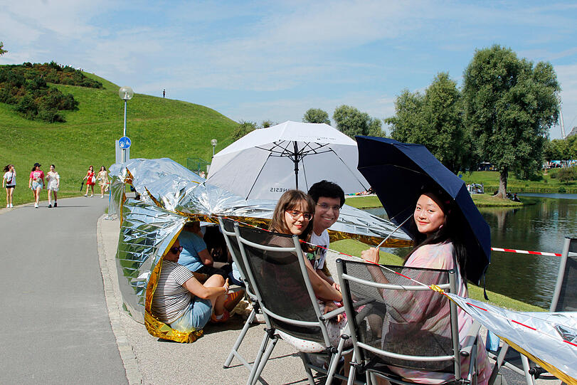 Gabriel (23) aus Pfaffenhofen, Edona (21) aus Pasing und Kieu (22) aus Freising machen es sich auf mitgebrachten Klappstühlen und Regenschirmen am Olympiasee gemütlich.