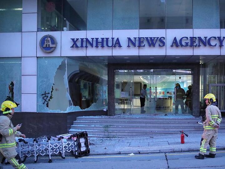 Einsatzkräfte der Feuerwehr stehen vor dem Gebäude der chinesischen Nachrichtenagentur Xinhua in Hongkong, dessen Fenster bei Protesten gegen die Regierung zerstört wurden.