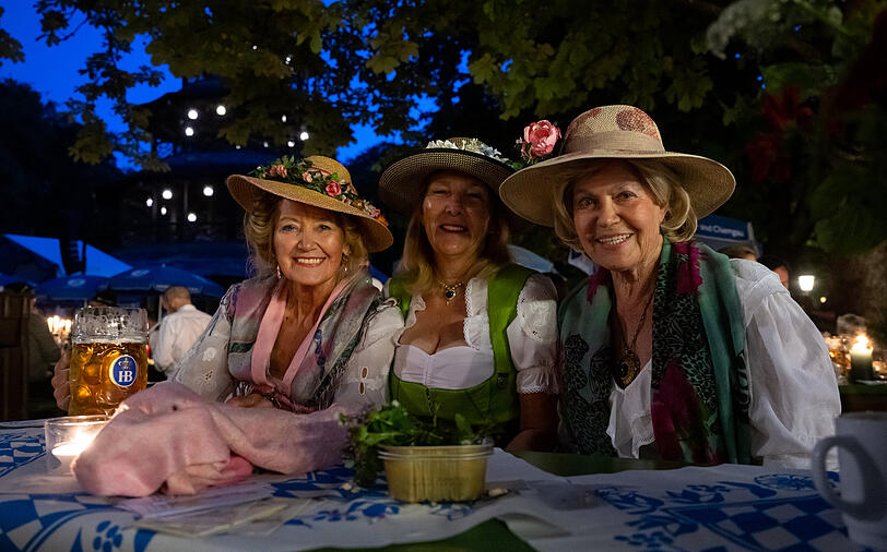 Drei Frauen sitzen beim traditionellen Kocherlball am Chinesischen Turm im Englischen Garten an einem Biertisch.
