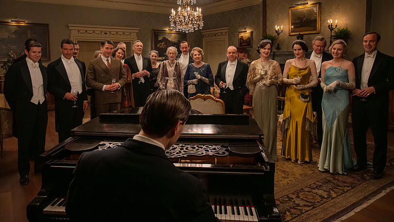 Allen Leech als Tom Branson, Dominic West als Guy Dexter, Robert James-Collier als Thomas Barrow, Douglas Reith als Lord Merton, Sarah Crowden als Lady Manville, Penelope Wilton als Isobel Merton, Paul Giamatti als Harold Levinson, Elizabeth McGovern als Cora Grantham, Michelle Dockery als Lady Mary, Hugh Bonneville als Robert Grantham, Laura Carmichael als Lady Edith und Harry Hadden-Paton als Bertie Hexham in „Downton Abbey: Das große Finale“.