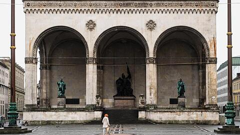 Eine Frau geht über den Odeonsplatz an der Feldherrnhalle vorüber. Foto: Matthias Balk/dpa/Archivbild
