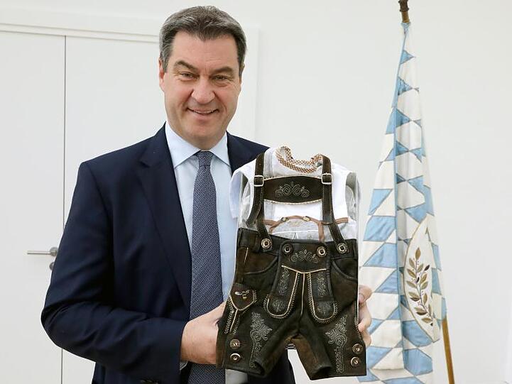 Markus Söder (CSU), Ministerpräsident von Bayern, zeigt eine Lederhose und ein Trachtenhemdchen für Kinder. Foto: Bayerische Staatskanzlei