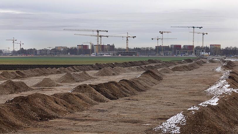Ende 2018: Hinter einer grünen Wiese an einer Großbaustelle in Freiham stehen Kräne.