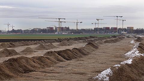 Ende 2018: Hinter einer grünen Wiese an einer Großbaustelle in Freiham stehen Kräne.