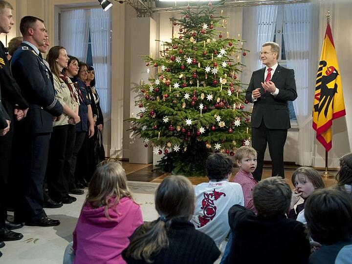 Christian Wulff bei seiner Weihnachtsansprache im großen Saal des Schlosses. Die Kinder sitzen vor ihm auf dem Teppich. Die Erwachsenen haben sich im Kreis aufgebaut.