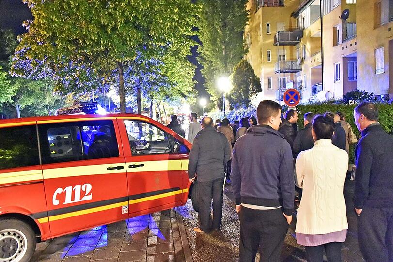 Bewohner des Mietshauses und etliche Schaulustige aus der Nachbarschaft drängen sich auf der Straße.