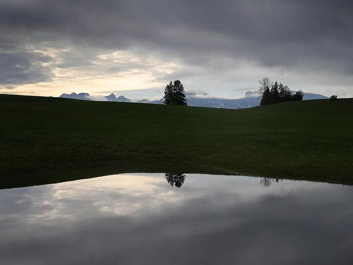 Der mit Wolken überzogene Himmel spiegelt sich in einer vom Regen überfluteten Wiese. Foto: Karl-Josef Hildenbrand/dpa/Archivbild