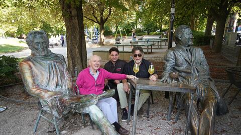 Noch ist Helmut Dietl am Café Münchner Freiheit neben dem Monaco Franze verhüllt. Die AZ durfte die Skulptur bereits unverhüllt fotografieren. Im Bild (v.l.): Kaffeehausgründer Karl Eisenrieder (83) mit Sohn Max Eisenrieder sowie Künstler Nikolai Tregor, der beide Skulpturen erschaffen hat.