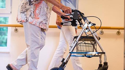 Eine Pflegekraft geht in einem Pflegeheim mit einer älteren Dame über einen Korridor. Künftig sollen Beschäftige in der Alten- und Krankenpflege besser bezahlt werden.