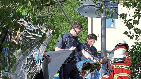Polizisten stehen hinter einem Polizei-Flatterband am Tatort in Murnau. Dort haben die Ermittler nach zwei mutmaßlichen Morden am Samstag großräumig abgesperrt.