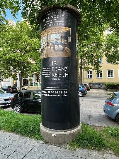 Auf einer Litfaßsäule in der Possartstraße klebt Werbung fürein anderes Luxus-Projekt von M-Concept: in Kitzbühel mit Blick auf die Streif.