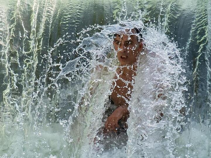 Ein Mann kühlt sich an einem kleinen Wasserfall im Eisbach im Englischen Garten ab.