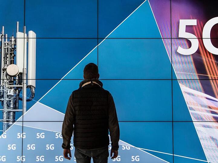 Ein Mann steht im Gebäude der Bundesnetzagentur vor einer Leinwand mit der Aufschrift "5G". Die Bundesnetzagentur versteigert 41 Frequenzblöcke an verschiedene Anbieter.