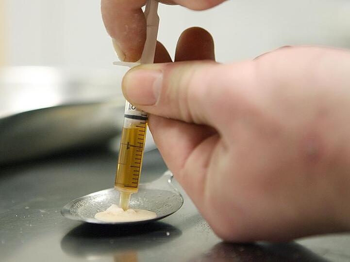 Ein Drogenkonsument zieht Heroin in eine Spritze. Foto: Boris Roessler/Archivbild